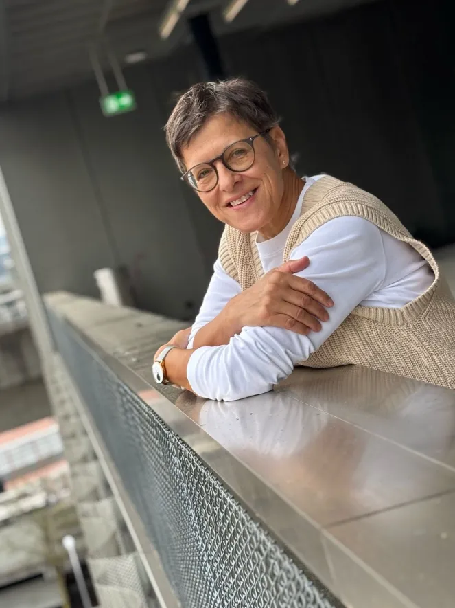 Frau lächelnd mit Brille, weissem TShirt und beigen Pullunder