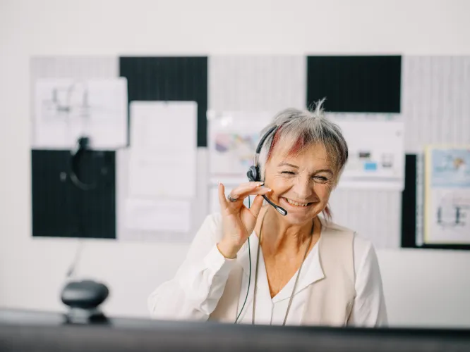 Ältere Frau mit Headset nimmt lächeln ein Telefon entgegen.